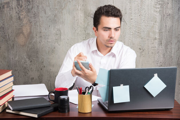 雇员办公室职员看着笔记本电脑 拿着电话在办公桌旁笔记本年轻人工作