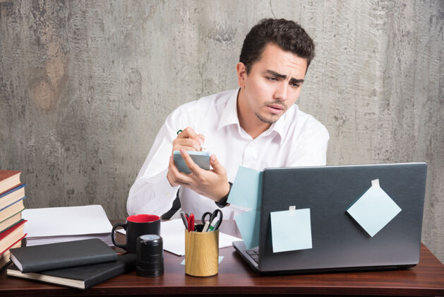 办公桌办公室职员看着笔记本电脑 拿着电话在办公桌旁工作笔记本男性