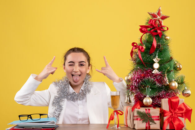健康正面图：女医生坐在黄色背景的桌子后面 还有圣诞树和礼品盒花新郎背景