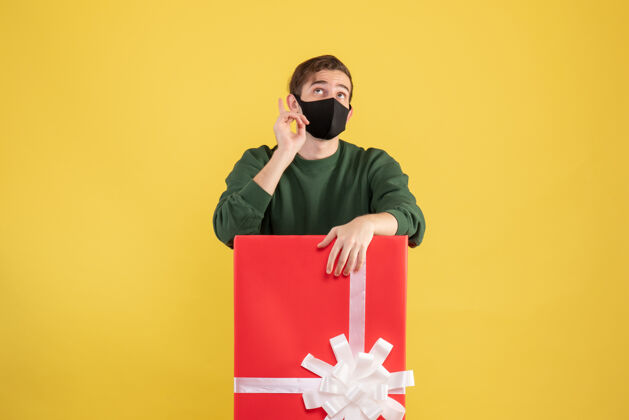 年轻正面图：年轻人站在黄色的大礼盒后面抬头看礼品盒商人面具