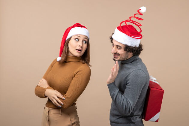 肖像新年心情有趣可爱的情侣戴着红色圣诞老人帽在灰色的舞台上互相交谈心情圣诞老人帽子