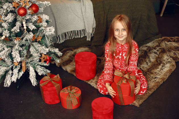 毛衣穿着红色睡衣的孩子坐在圣诞树旁的女儿家玩具快乐