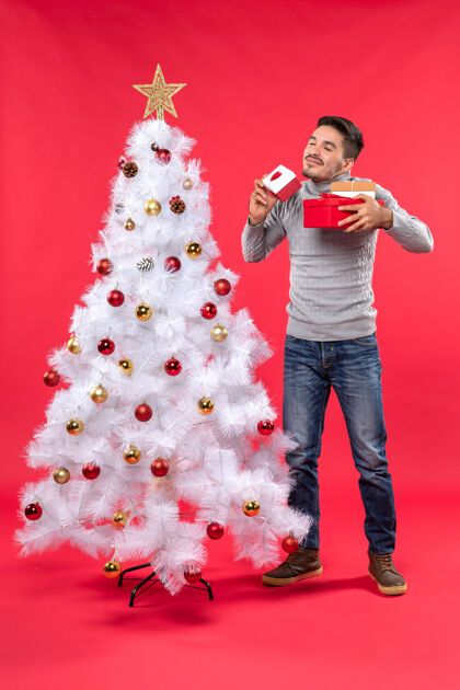 衬衫站在装饰过的白色圣诞树旁的穿着灰色上衣的帅哥大人的俯视图上衣站着圣诞树