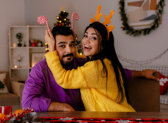 圣诞年轻漂亮的夫妇 男人和女人 拿着糖果手杖 在圣诞装饰的房间里一起快乐地恋爱 背景是圣诞树糖果有乐趣