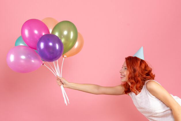 聚会粉红色墙上手持彩色气球的年轻女子的正视图年轻的女性丝带乐趣