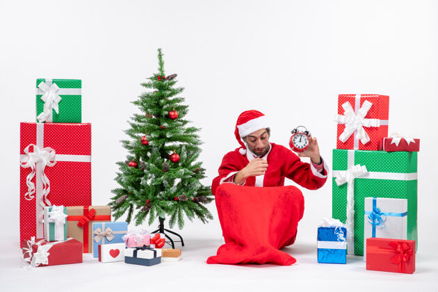 年轻人年轻人坐在地上庆祝圣诞节 并在礼物和圣诞树旁展示钟表展示礼物地