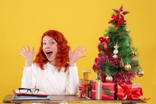树女工人坐在桌子后面 手里拿着圣诞树和黄色的礼物黄色礼物圣诞节