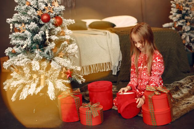 坐穿着红色睡衣的孩子坐在圣诞树旁的女儿圣诞树美丽