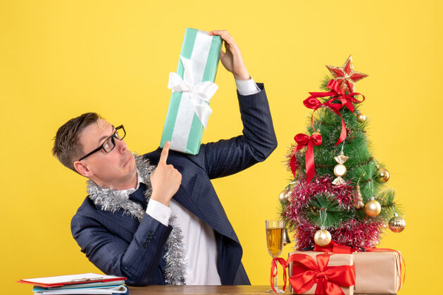 礼物在圣诞树旁的桌子旁 好奇的男人正在检查礼物 黄色的礼物人圣诞节好奇的人