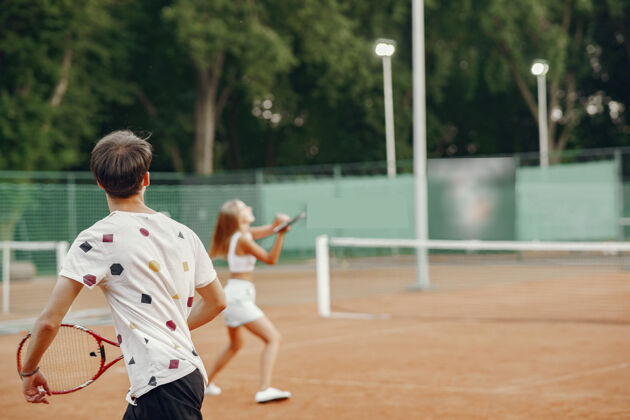 男人网球场上的一对年轻夫妇两个穿着运动服的网球运动员户外球拍练习