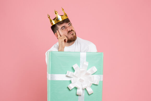 皇冠礼物盒内年轻人的正面图 粉色墙上有王冠思考礼物男性快乐