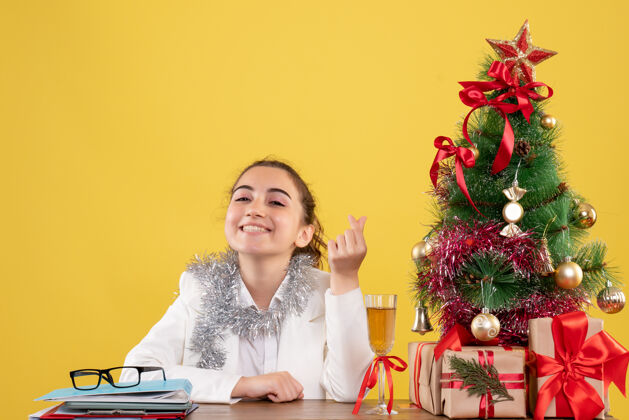 圣诞节正面图：女医生坐在黄色背景的桌子后面 还有圣诞树和礼品盒医生插花情绪