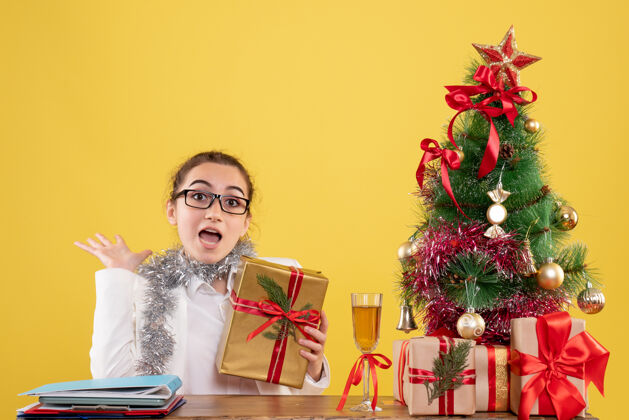 坐正面图女医生围坐在黄色背景上的圣诞礼物和圣诞树旁香水女性树