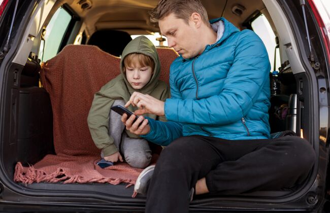 冒险父子俩在车里带着智能手机在公路上旅行汽车父亲孩子
