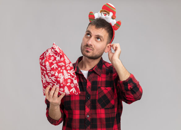 头带体贴的白人年轻人戴着圣诞头带 拿着圣诞袋 抚摸着耳朵 在白色的背景下孤零零地仰望耳朵抱感动