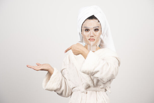 水疗穿着浴衣和带面罩的毛巾的女人漂亮面膜白色