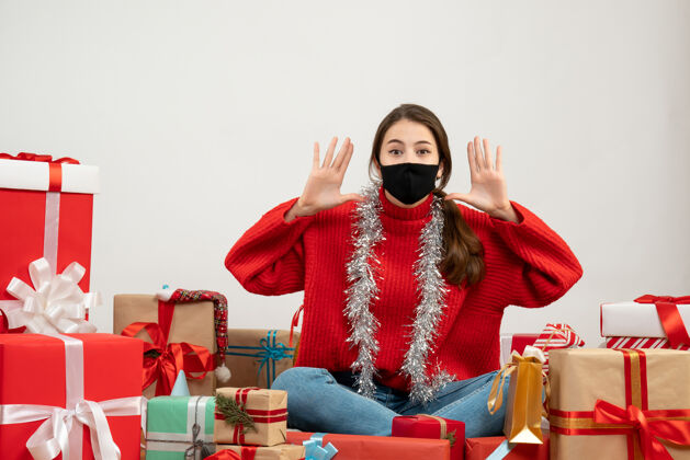 年轻穿着红色毛衣 戴着黑色面具的年轻女孩叫着坐在旁边的人送白色的礼物礼物圣诞节年轻女孩