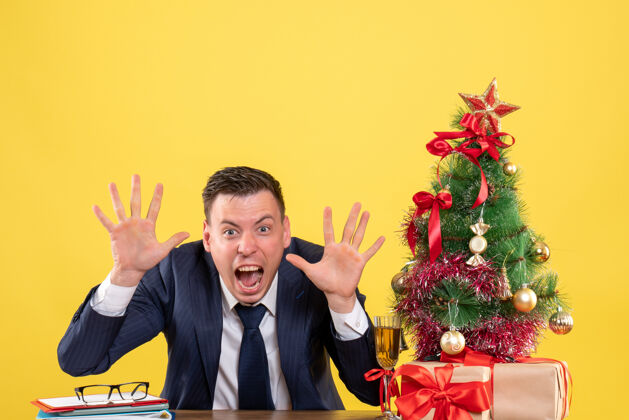 新郎正面图：年轻人坐在圣诞树旁的桌子旁 黄色的礼物桌子圣诞节树