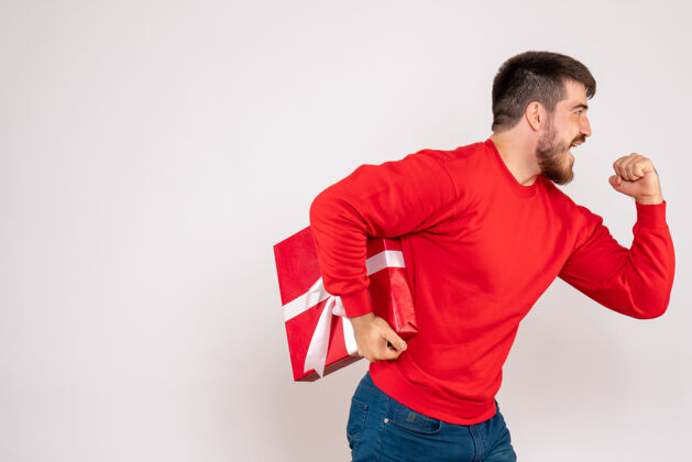 抱一个穿着红衫的年轻人拿着圣诞礼物站在白色的墙上年轻的男人帅哥男人