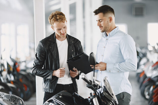 服务男人在摩托店里选摩托车穿黑色夹克的家伙经理和客户在一起年轻摩托车手购买