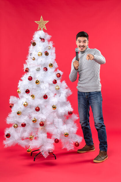 站着新年气氛积极的家伙穿着牛仔裤站在装饰圣诞树附近肖像牛仔裤圣诞树