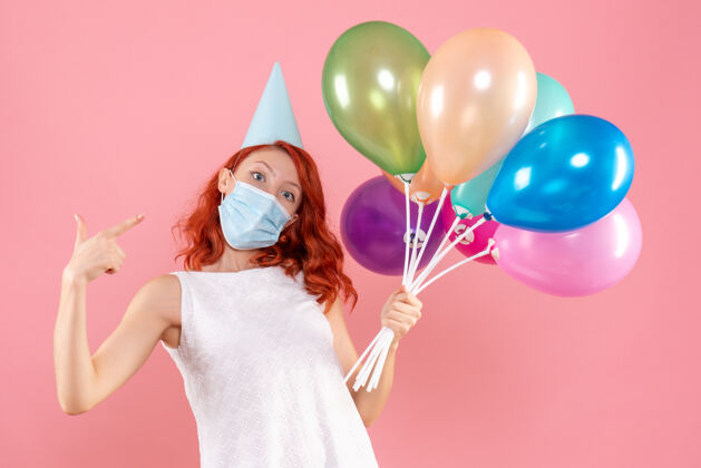 举行前视图中的年轻女子拿着五颜六色的气球在无菌面具上粉红色的墙壁生日粉色五颜六色