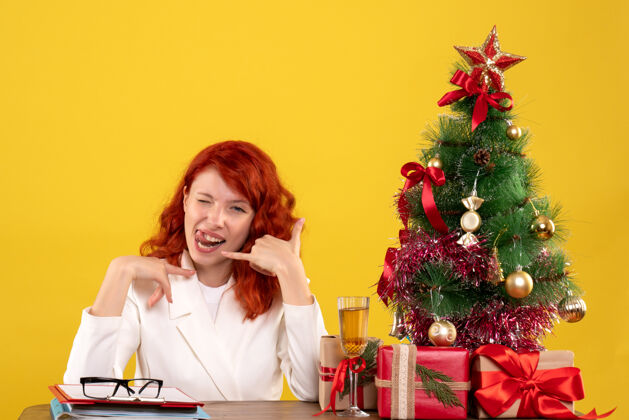 礼物女工人坐在桌子后面 手里拿着圣诞礼物和黄色的圣诞树女黄色桌子