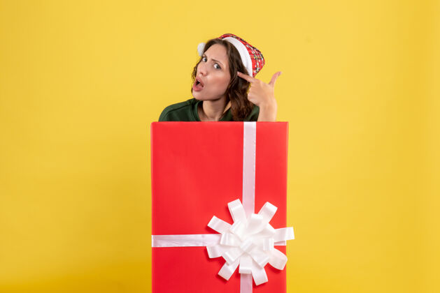 站立站在黄色墙上盒子里的年轻女子的正视图圣诞节节日礼物
