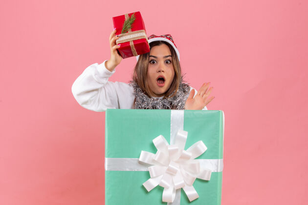 举行礼物盒内的年轻女子正面图 粉红色墙上拿着小礼物小快乐十二月