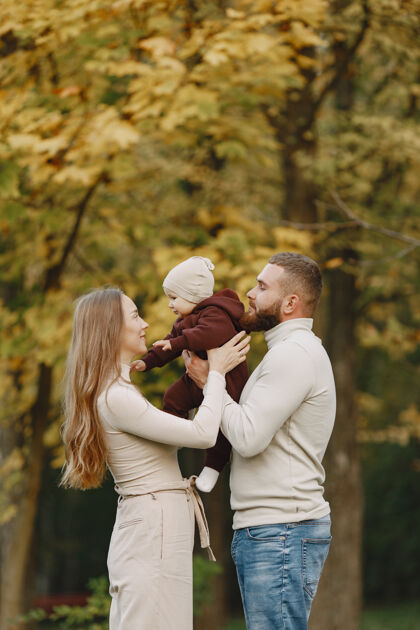 成人秋天公园里的一家人穿棕色毛衣的男人和父母在一起的可爱小女孩聚在一起衣服头发