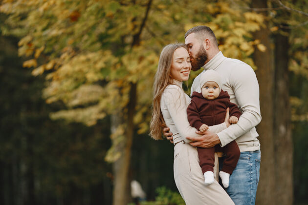 三个秋天公园里的一家人穿棕色毛衣的男人和父母在一起的可爱小女孩微笑父母户外