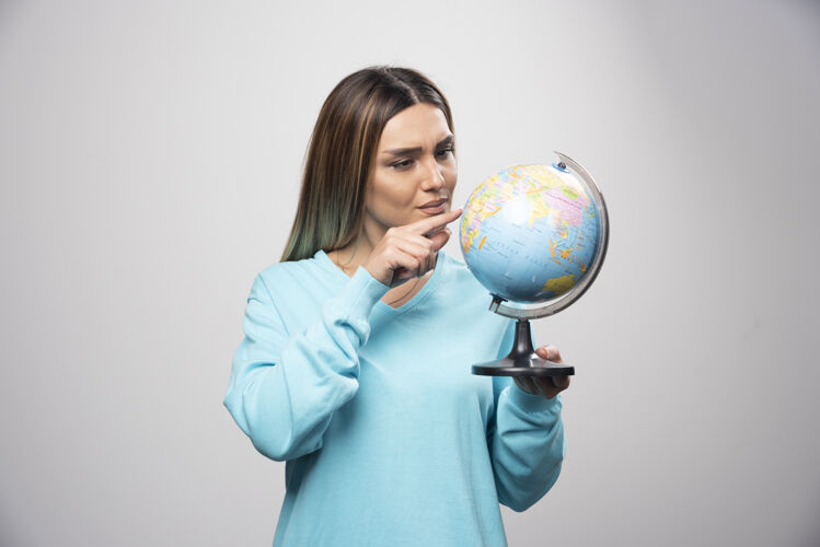 地图穿着蓝色运动衫的金发女孩拿着一个地球仪 猜着地点 玩得很开心地球世界年轻人