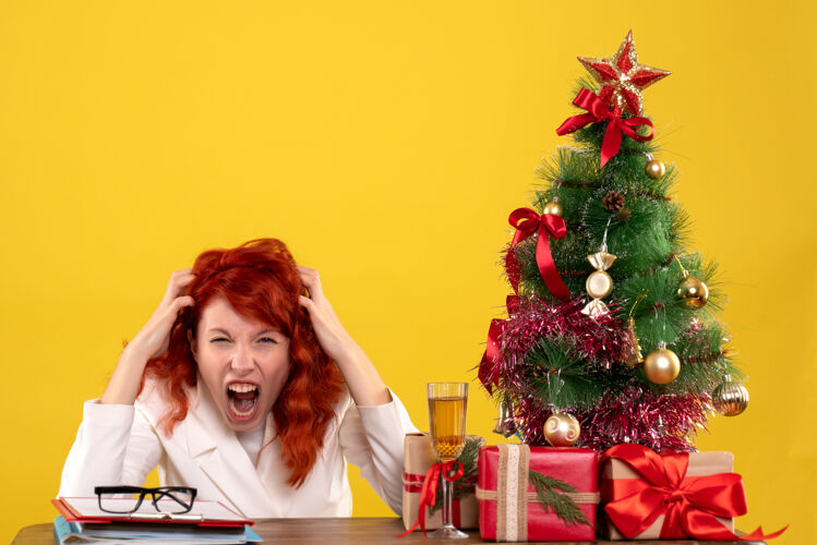 安排女工人坐在桌子后面 手里拿着圣诞礼物 树在黄色上尖叫树女工黄色