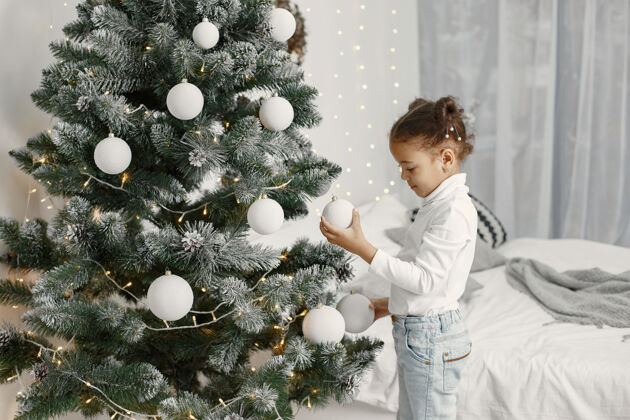 小穿白色毛衣的孩子站在圣诞树旁的女儿节日年轻圣诞节