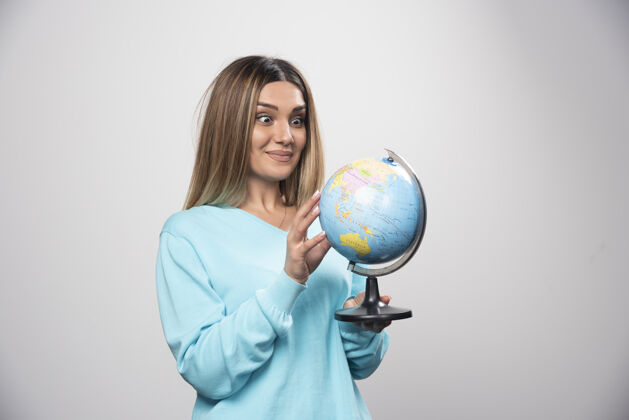 积极穿着蓝色运动衫的金发女孩拿着一个地球仪 猜着地点 玩得很开心旅行金发休闲