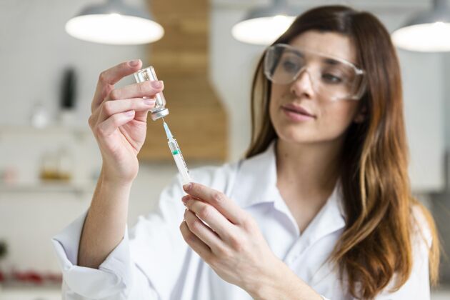 化学家戴着安全眼镜的女科学家在实验室里拿着装有疫苗的注射器炼金术化学研究