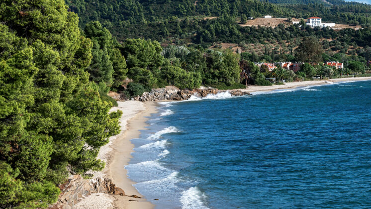 南部希腊爱琴海海岸 多岩石的山上长着树木和灌木 海滩上有海浪 建筑物位于海岸附近山海湾海岸线