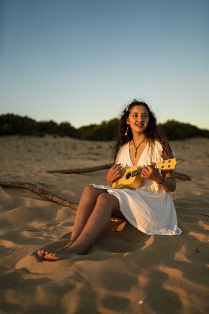 音乐一个穿着白色裙子坐在沙地上微笑的女性的垂直镜头女人木头声音