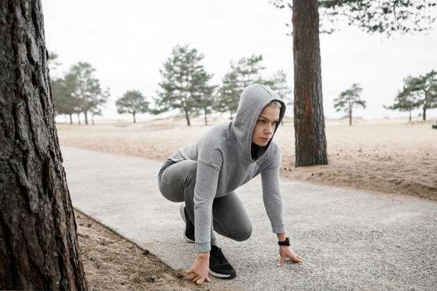 开始运动 健身 健康 健康 活力和竞争理念户外形象的集中年轻女运动员在连帽衫和运动鞋坐在稳定的立场上铺砌的小径 准备运行健身训练连帽衫