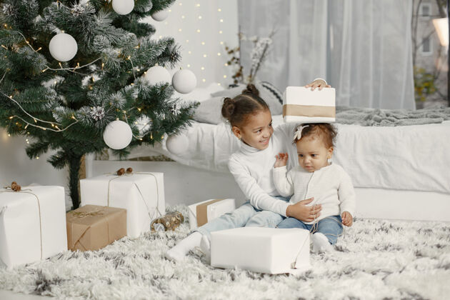 节日穿着白色毛衣的孩子女儿们在圣诞树旁缝线两个姐妹在家童年毛衣小