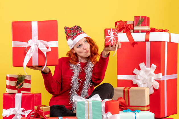 圣诞节坐在黄色墙上的圣诞礼物周围的年轻女子的正视图前面礼物节日