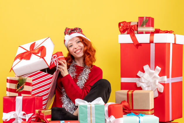 快乐坐在黄色墙上的圣诞礼物周围的年轻女子的正视图坐着盒子购物