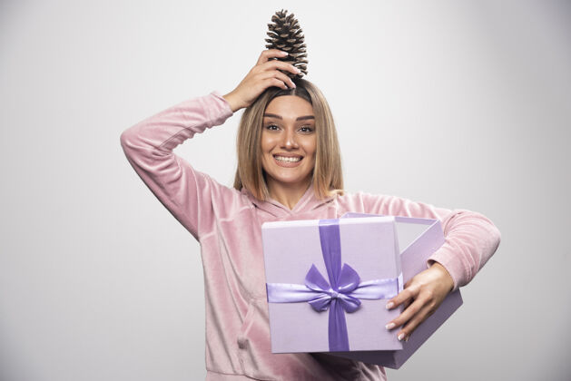 礼品盒穿着粉色运动衫的金发女士从礼盒里拿出一个橡树锥 感觉很高兴礼物积极女士