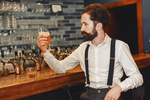 肖像一个留着胡子的男人站在吧台旁 喝着酒杯里的酒酒精帅哥表情