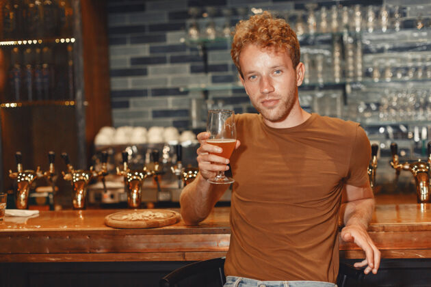白兰地有魅力的年轻人站在吧台后面一个穿着棕色t恤的男人手里拿着一个玻璃杯马克杯西装酒