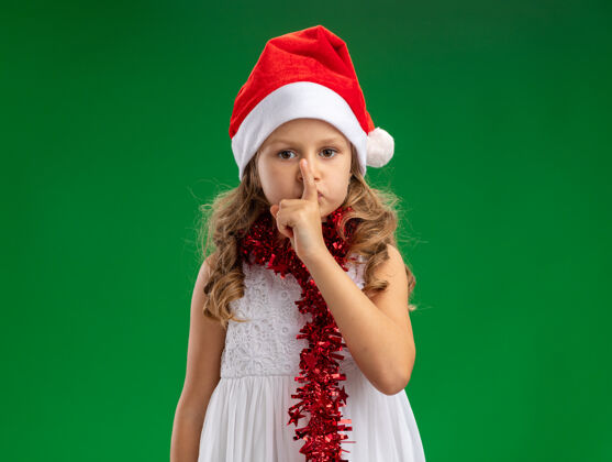 沉默小女孩戴着圣诞帽 脖子上戴着花环 在绿色的背景下表现出沉默的姿态圣诞节未发布帽子