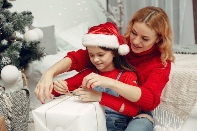 给予人们在为圣诞节做准备母亲在和女儿玩耍一家人在节日的房间里休息孩子穿着红色毛衣女儿童年杉木