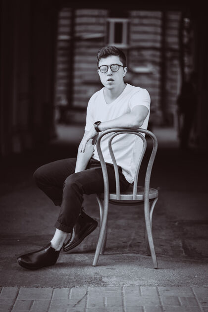 肖像街上穿着白色t恤 戴着墨镜坐在椅子上的男人的画像太阳乐趣城市