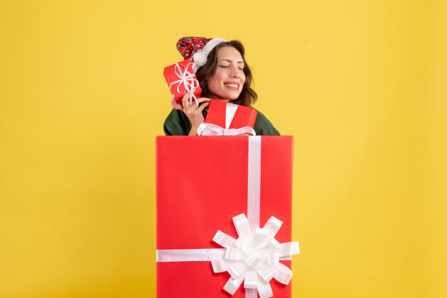 人站在盒子里的年轻女子的正面图 黄色的墙上有圣诞礼物里面快乐节日