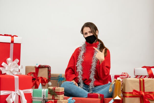 圣诞节穿着红色毛衣的年轻女孩指着自己围坐在白色的礼物旁边肖像红色欢快
